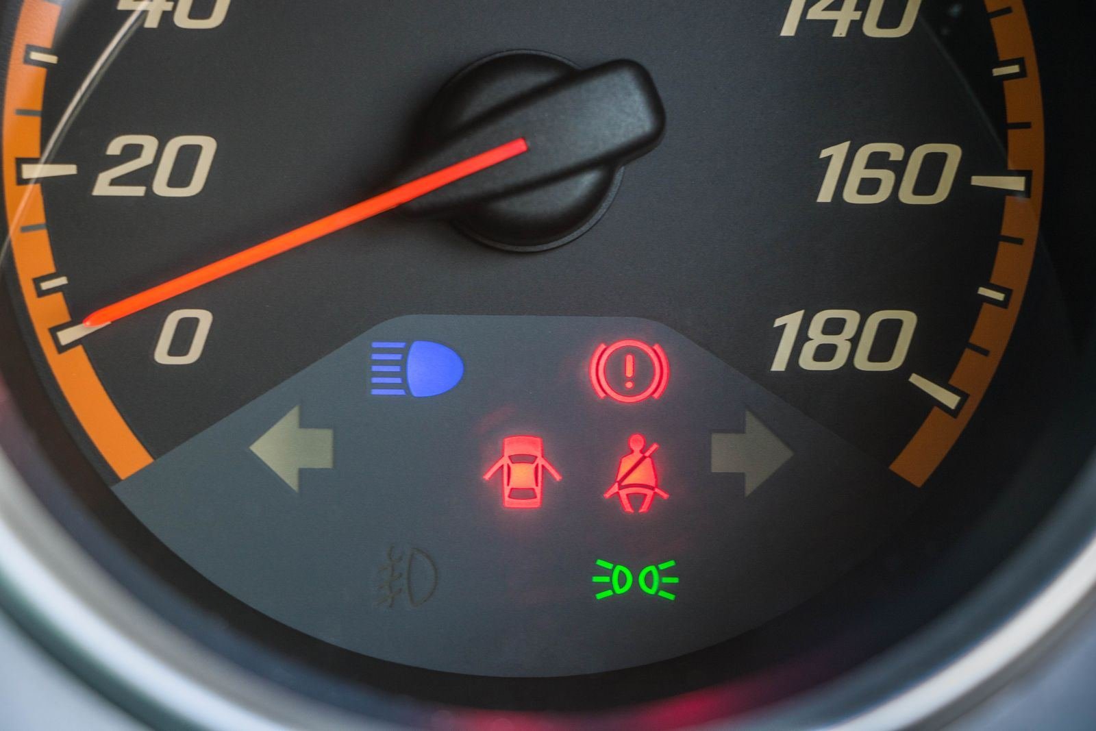 Speedometer showing red brake, door and seatbelt warning lights, a blue high-beam light and a green sidelight indicator